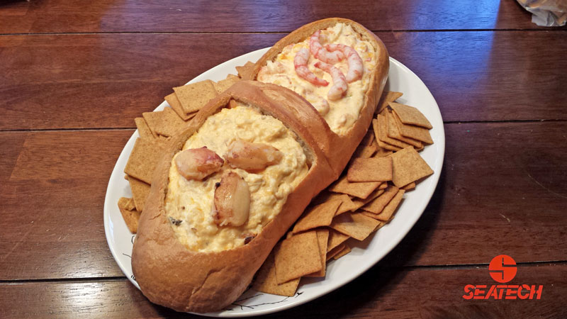 A photograph of crab dip and shrimp dip in a hallowed out loaf of french bread on a plate with crackers.