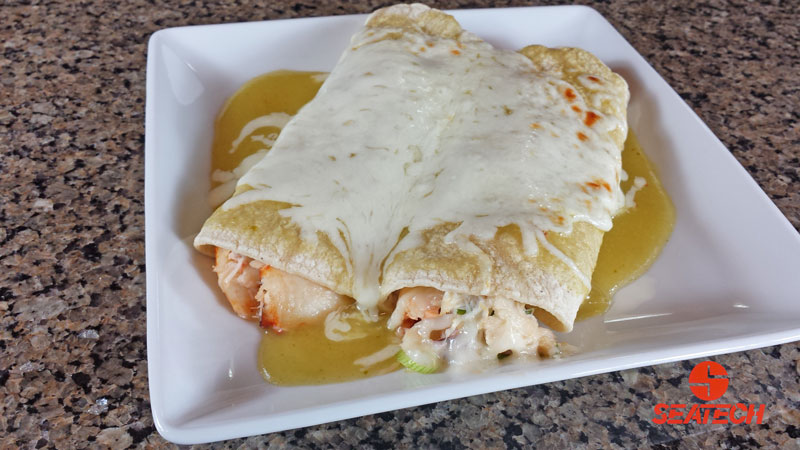 A photograph of Chilean crab meat enchiladas with melted cheese and green enchilada sauce.