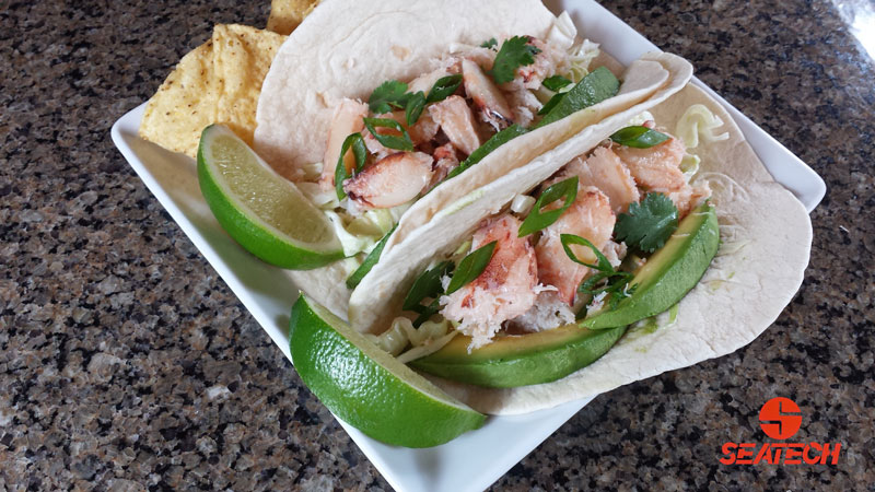 A phtograph of crab tocaos with crab meat, cabbage, sour cream, cilantro, green onions, avocaodo and sliced limes