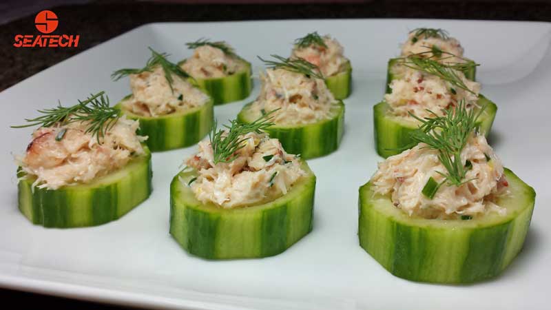 A photograph of sliced English cucumbers stuffed with crab salad and topped with a sprig of fresh dill.