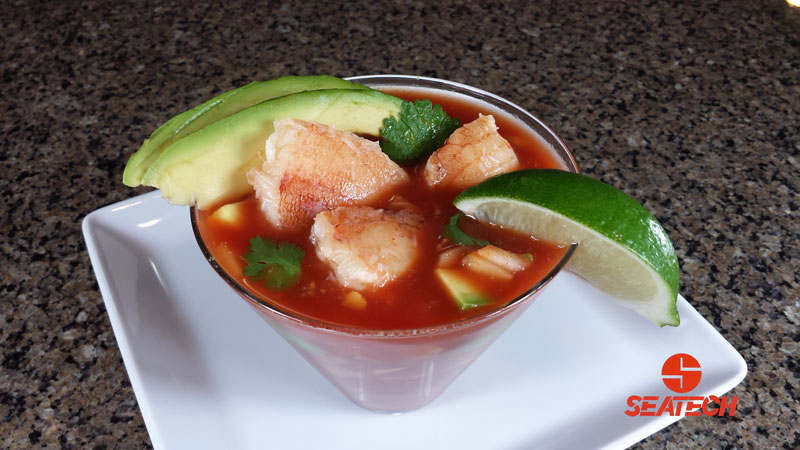A photograph of a crab mexican cocktail with crab meat, avocado, cucumber, cilantro, onion in a tomato juice mixture.
